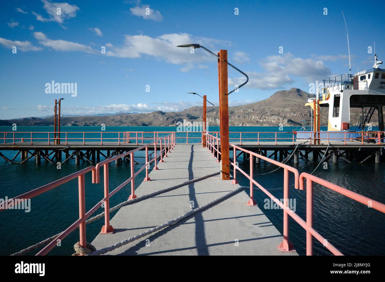 Entrance to jetty, on Lago General Carrera lake, Puerto Ibanez, Aysen, Chile. Pier with street lamps, mooring ropes crosses pier and moored ferry Stock Photo