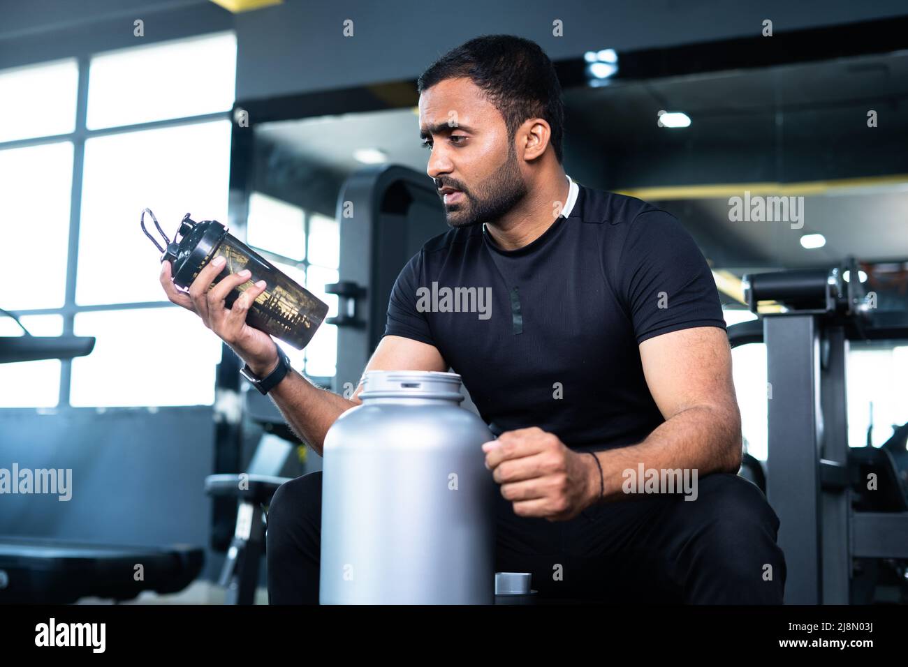 bodybuilder drinking protein by shaking bottle after gym workout