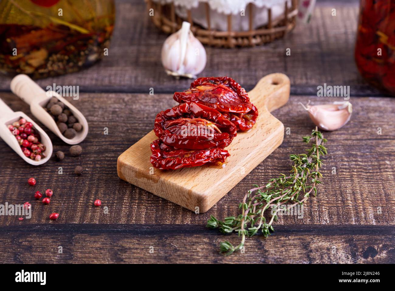 Sun-dried tomatoes in olive oil on a mini board with pepper, garlic and thyme in a rustic style. Selective focus, close-up. Stock Photo
