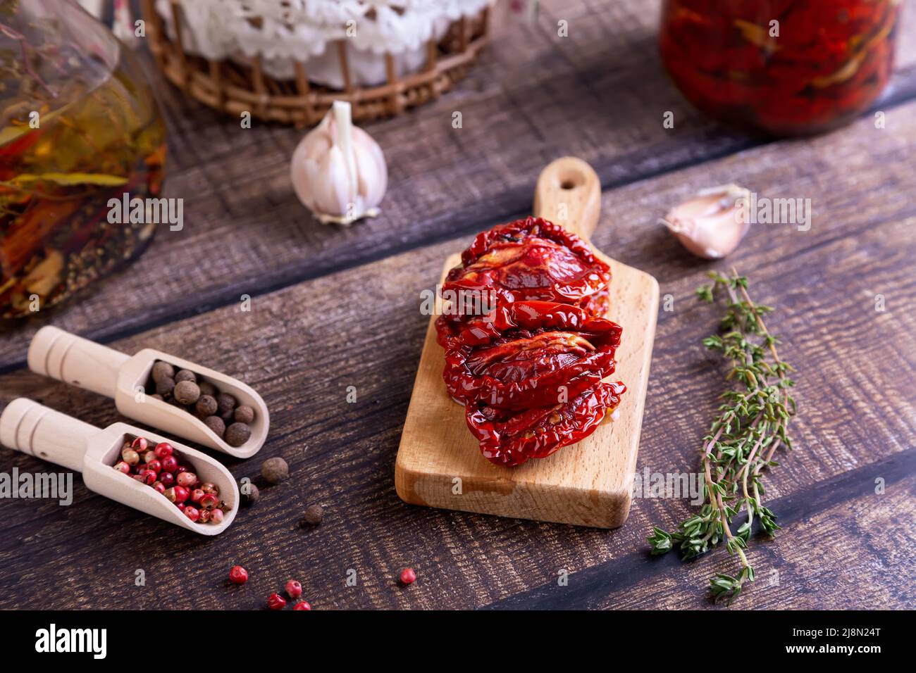 Sun-dried tomatoes in olive oil on a mini board with pepper, garlic and thyme in a rustic style. Selective focus, close-up. Stock Photo