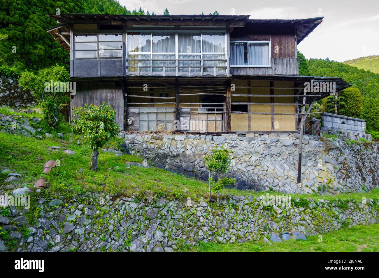 Exterior front view of old Japanese house with large windows and stone foundation in rural mountains Stock Photo