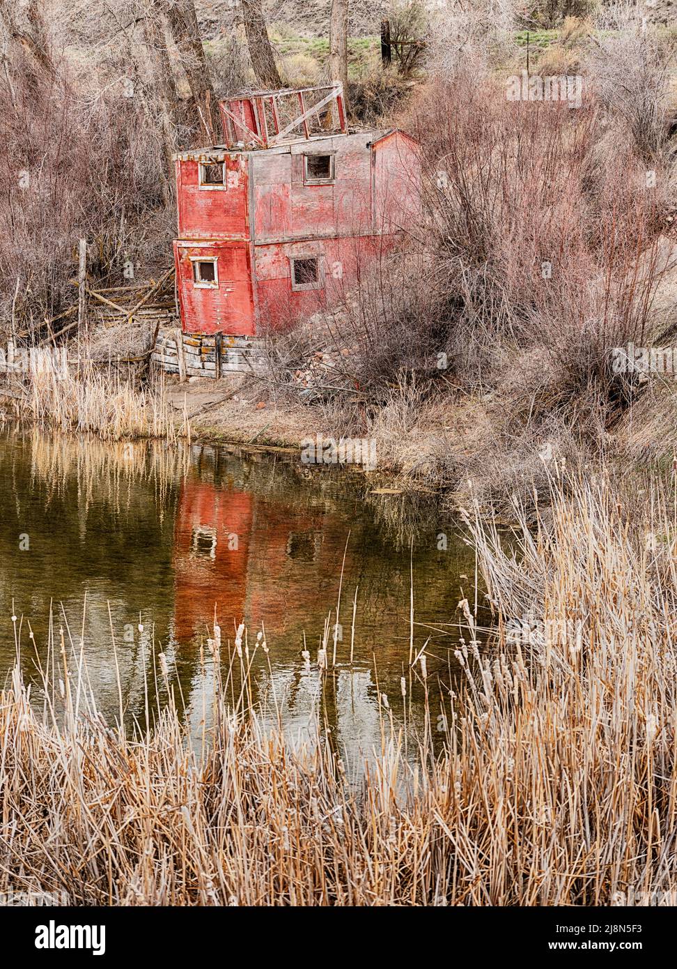 An old red fishing cabin is located next to a small pond in Colorado. Stock Photo