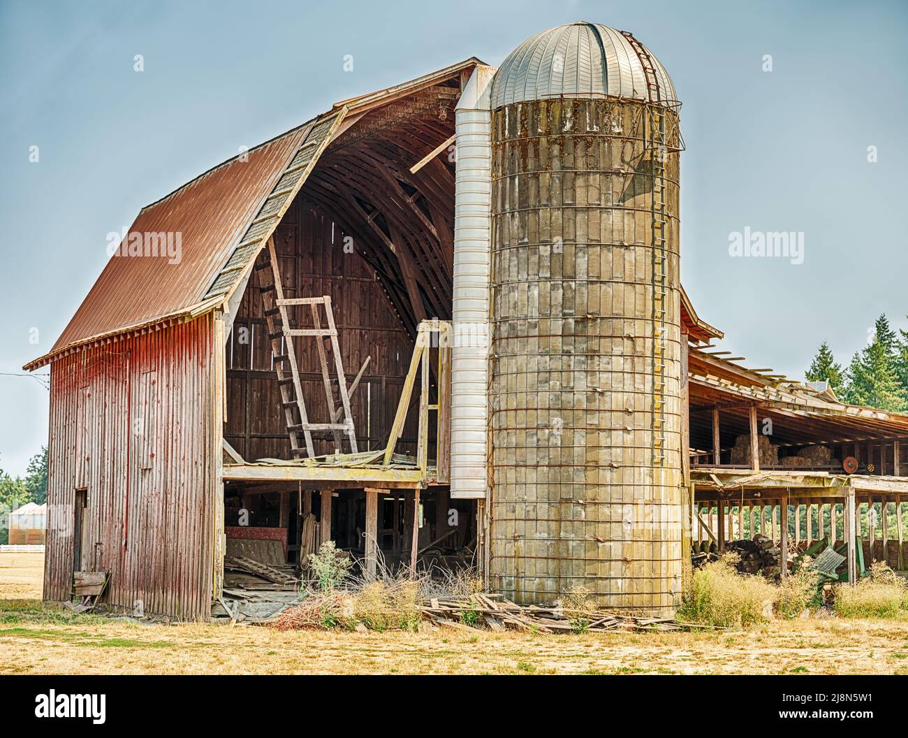 A concrete silo stands next to a barn with an open side wall. Stock Photo