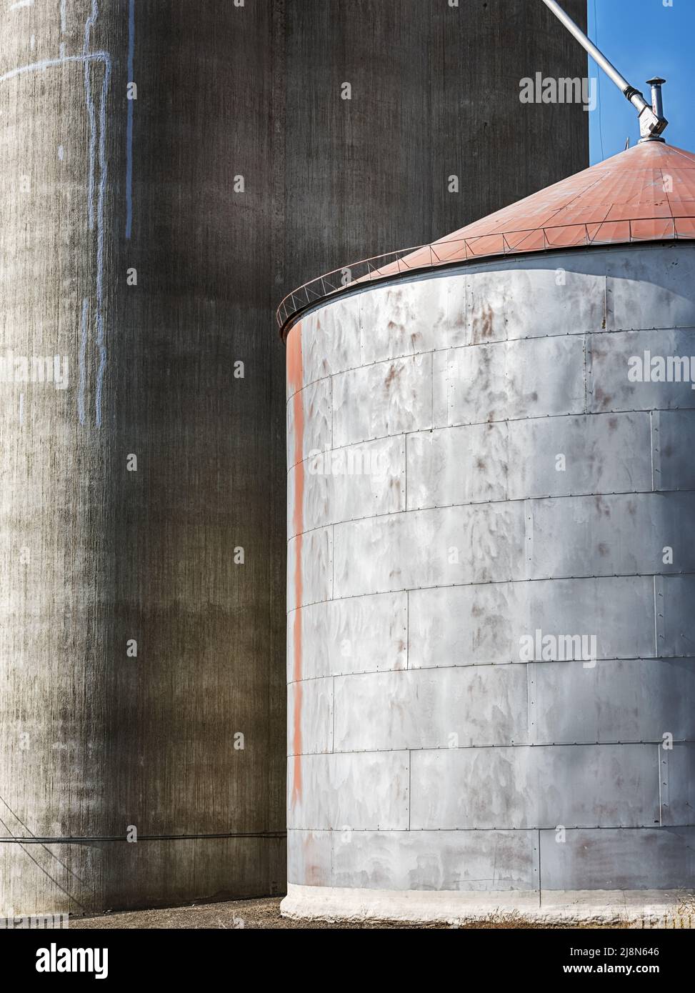 A large concrete grain elevator stands just behind a smaller metal storage facility in a rural scene near Govan, Washington. Stock Photo