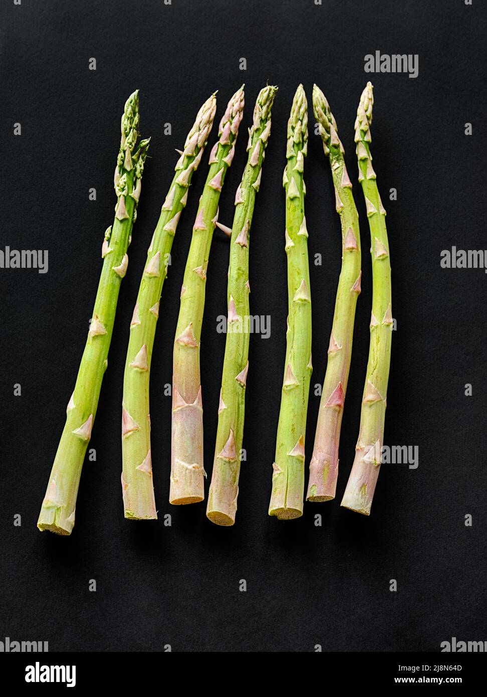 Seven asparagus spears are laid out against a black background. Stock Photo