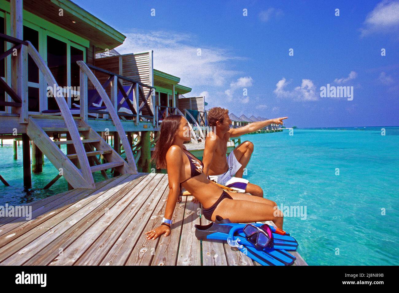 Couple sitting on a platform at the over-water bungalows, Kuredu, Laviyani Atoll, Indian Ocean, Asia Stock Photo