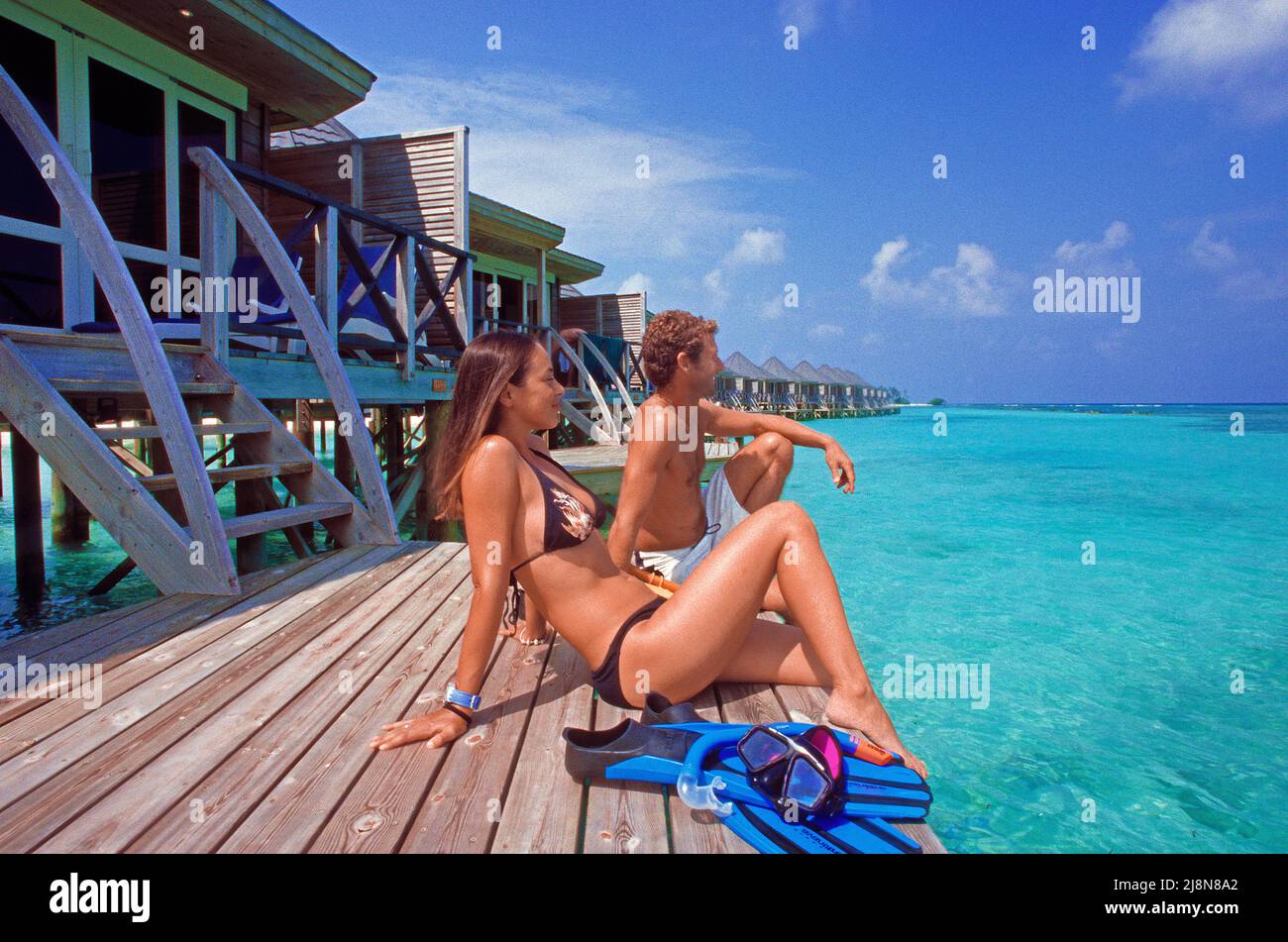 Couple sitting on a platform at the over-water bungalows, Kuredu, Laviyani Atoll, Indian Ocean, Asia Stock Photo