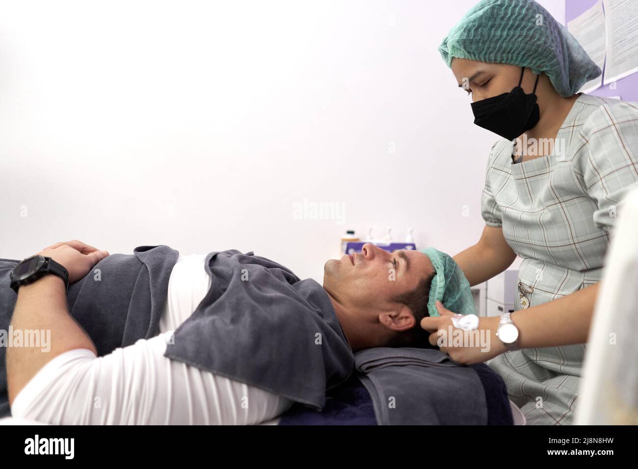 Nurse preparing a patient lying on a stretcher for rejuvenation treatment in a clinic Stock Photo