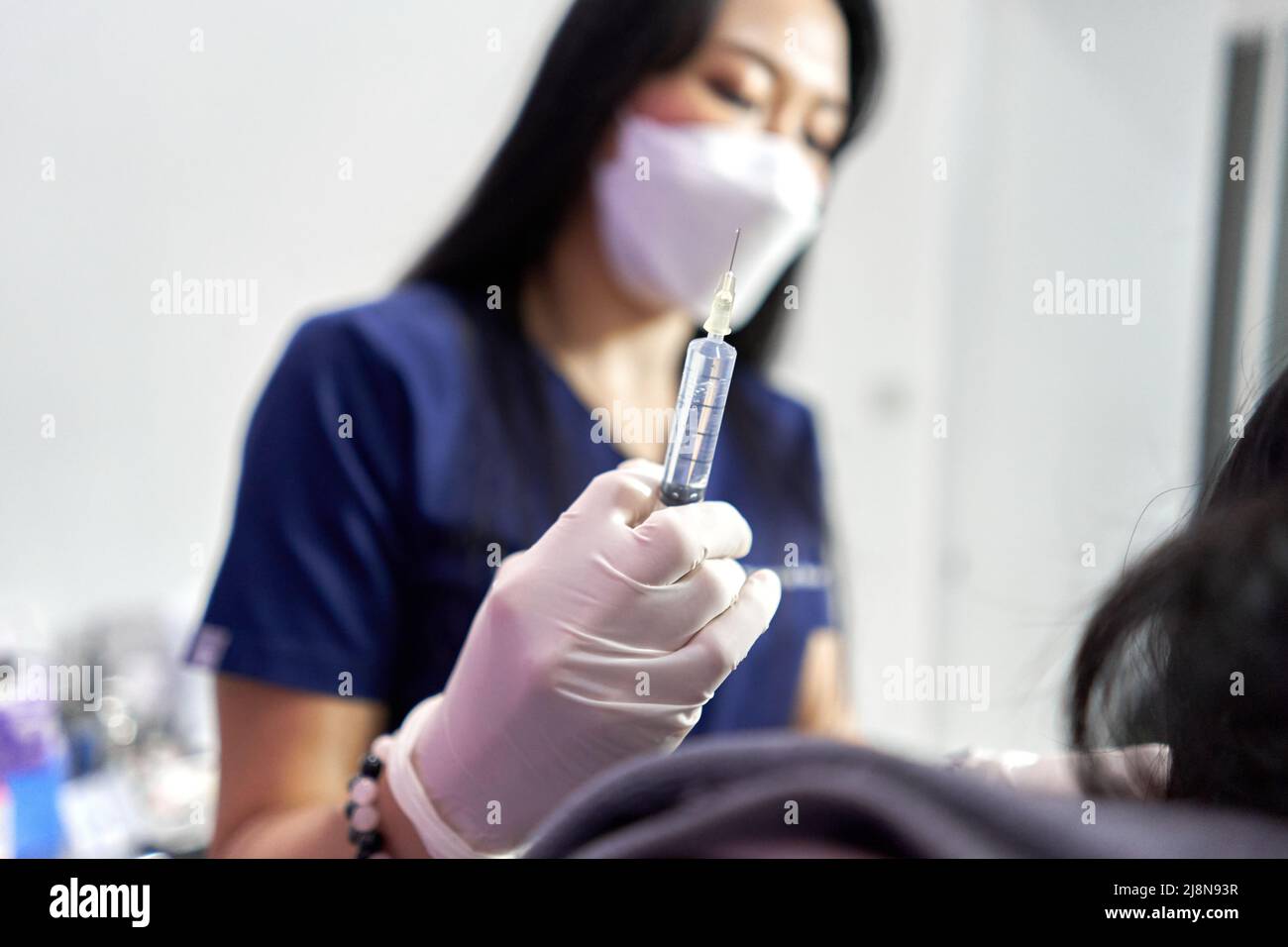 Focus on the hand of a doctor holding a botox injection for a patient Stock Photo