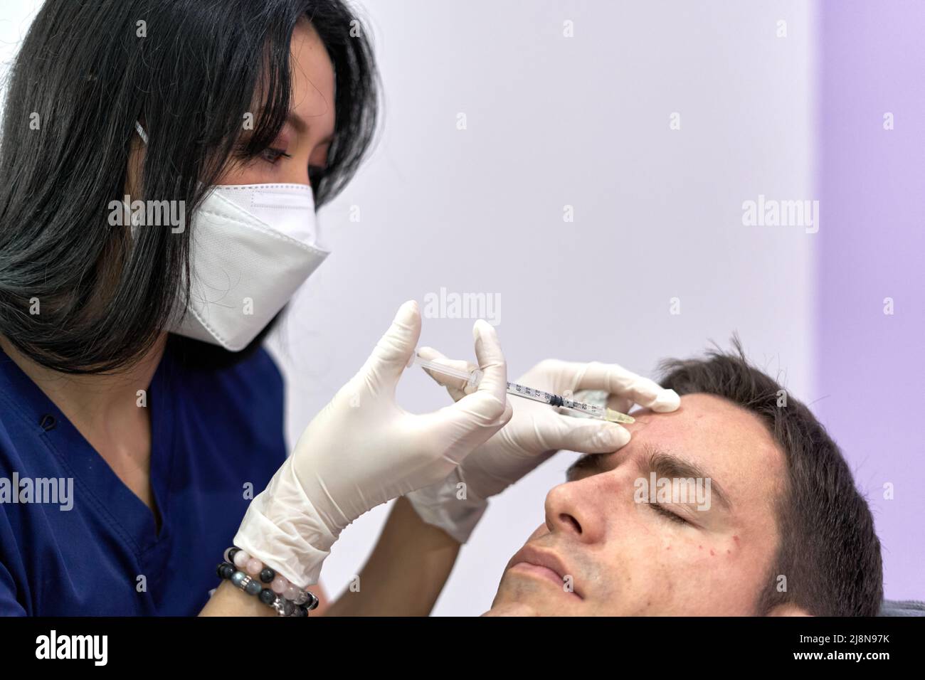 A doctor injecting collagen into a man's forehead to rejuvenate his face Stock Photo