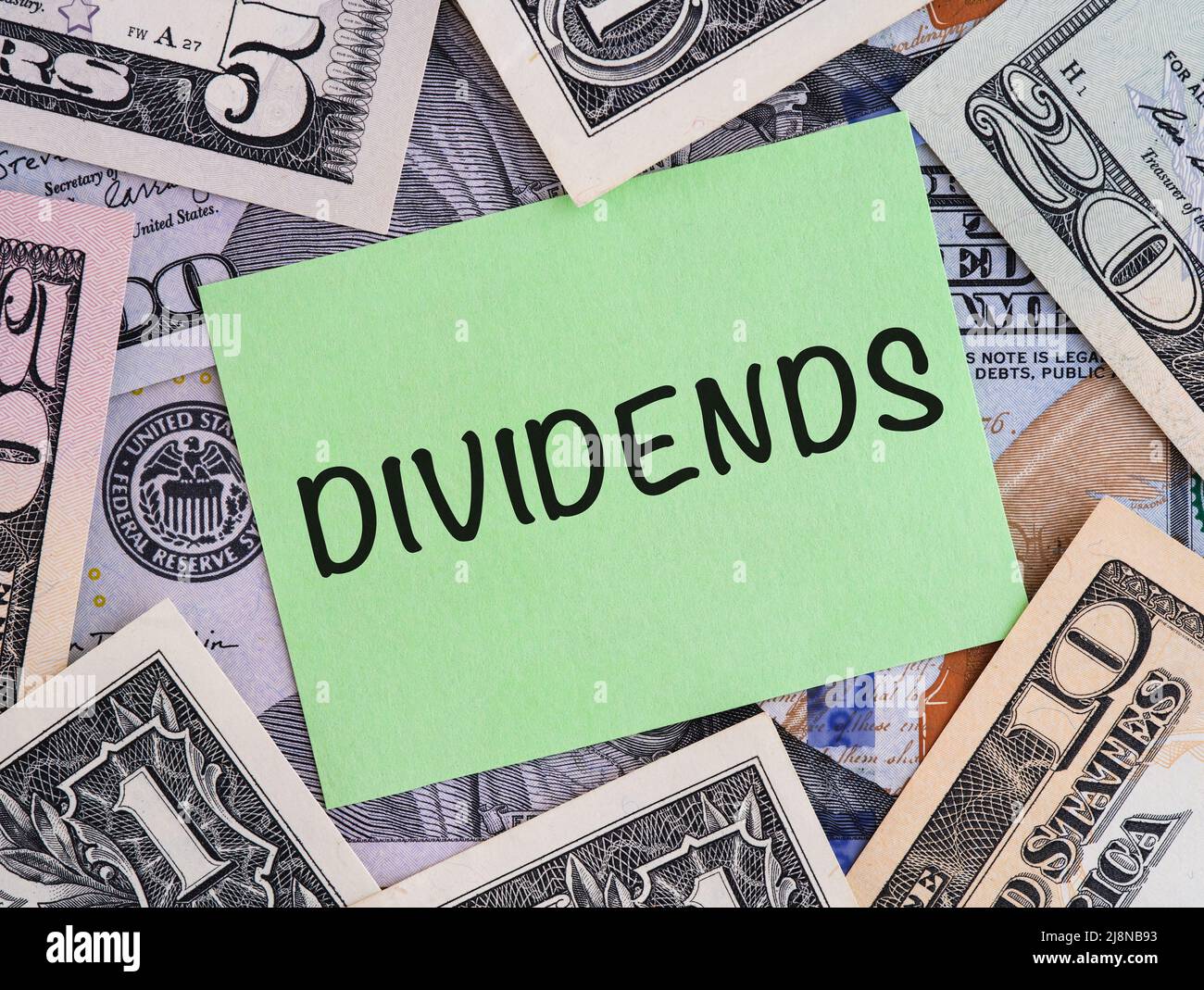 A Green paper note with word Dividends on a United States Dollar bills background. Stock Photo