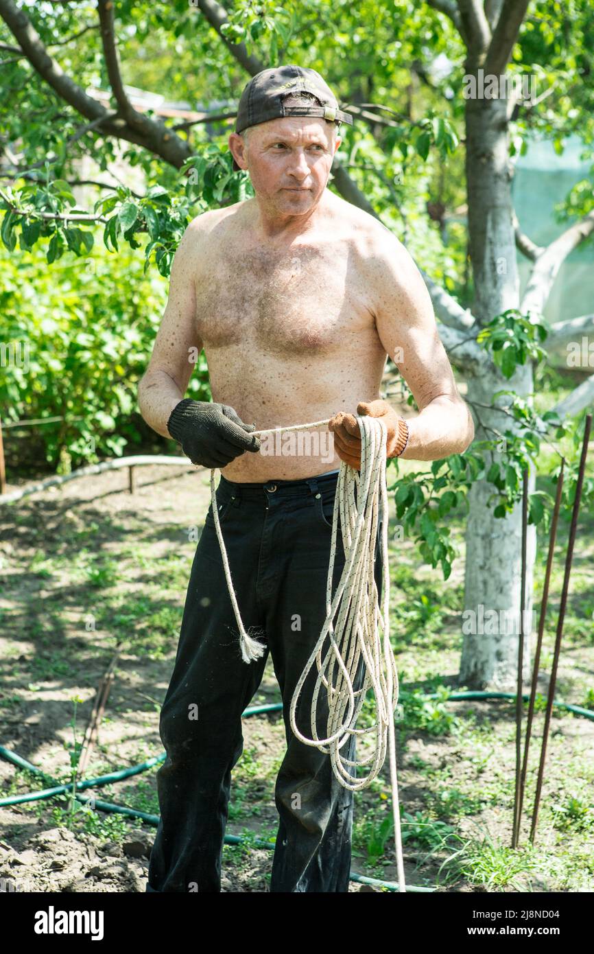 A man of mature years on a personal plot winds a rope for construction ...