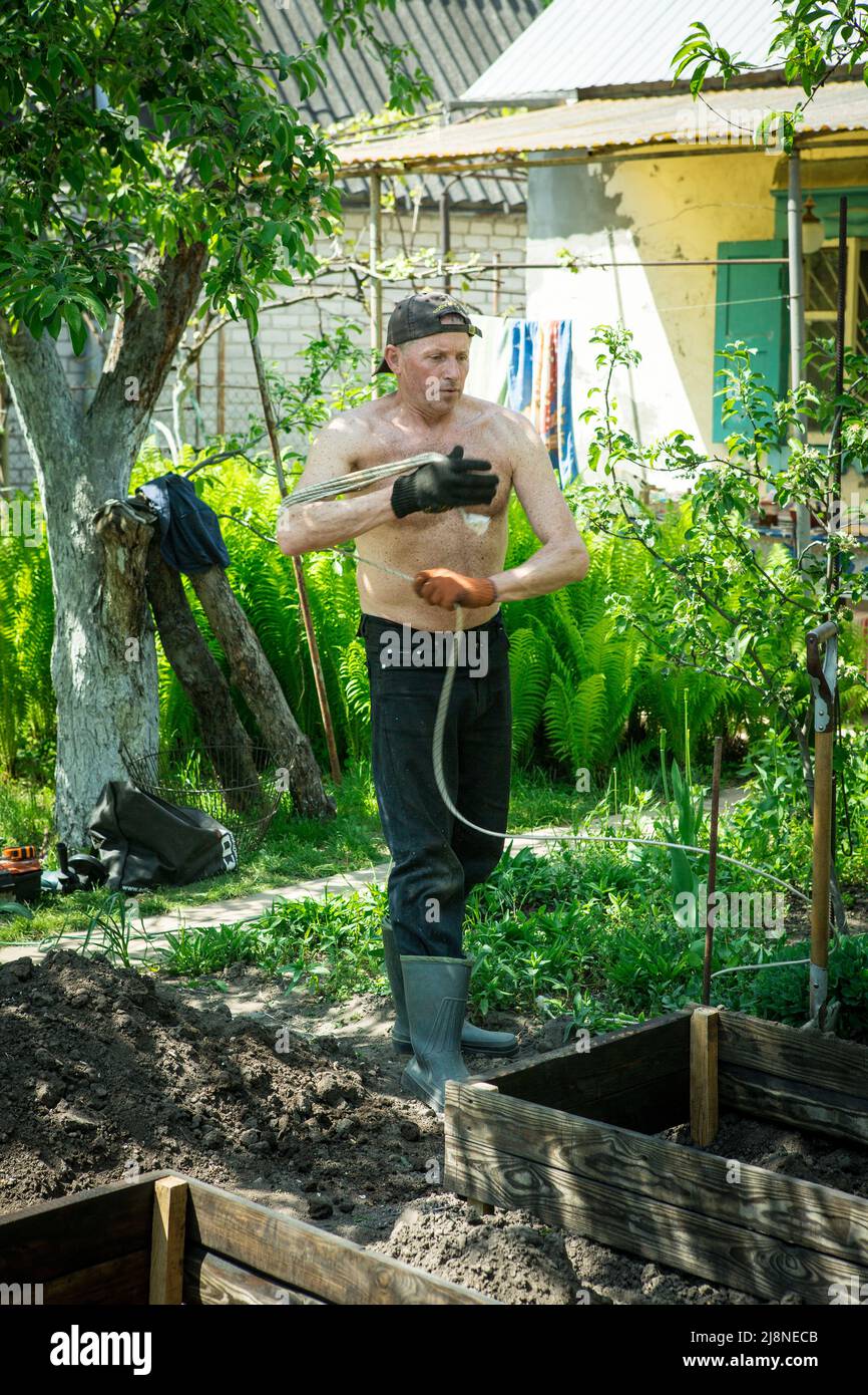 A man of mature years on a personal plot winds a rope for construction ...