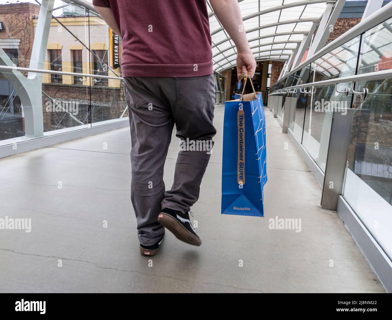 Bellevue, WA USA - circa April 2022: Low angle view of a man walking with a bag from The Container Store while wandering the Bellevue Mall Stock Photo