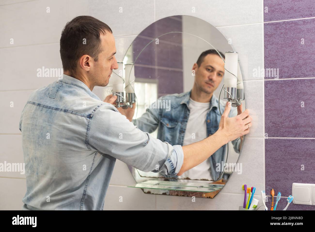Handyman installing a mirror in bathroom Stock Photo Alamy