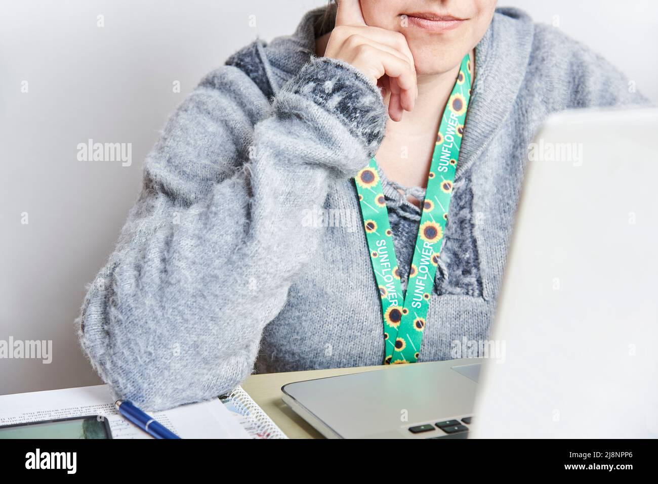 Unrecognizable woman looks at a laptop computer, studying or working at home, using a sunflower lanyard, symbol of people with invisible or hidden dis Stock Photo