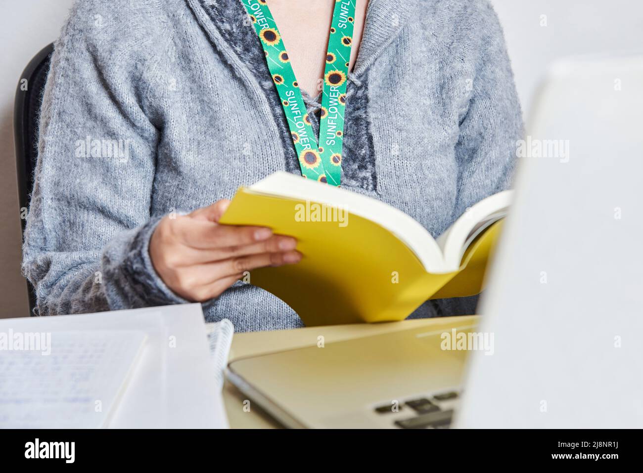 Unrecognizable woman reading a yellow book, studying or working at home, using a sunflower lanyard, symbol of people with invisible or hidden disabili Stock Photo