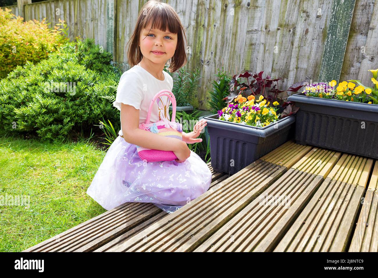 A cute smiling child is playing in the backyard with small pink bag. Sunny day. Good weather Stock Photo