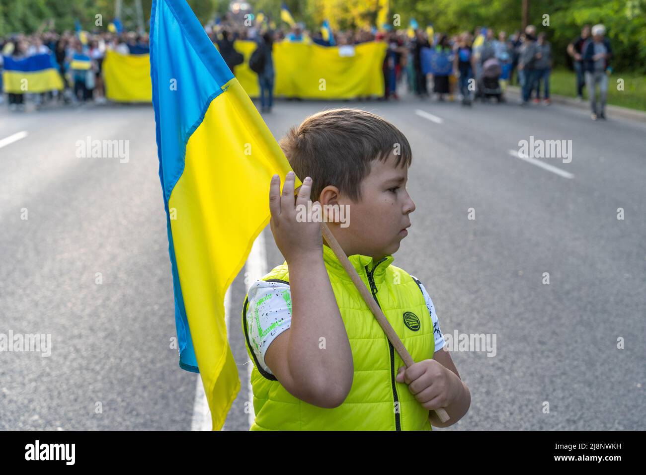 Sofia, Bulgaria - May 09, 2022: A kid with Ukrainian flag in his hands stands in front of a line of the people walking with a giant flag of Ukraine in Stock Photo
