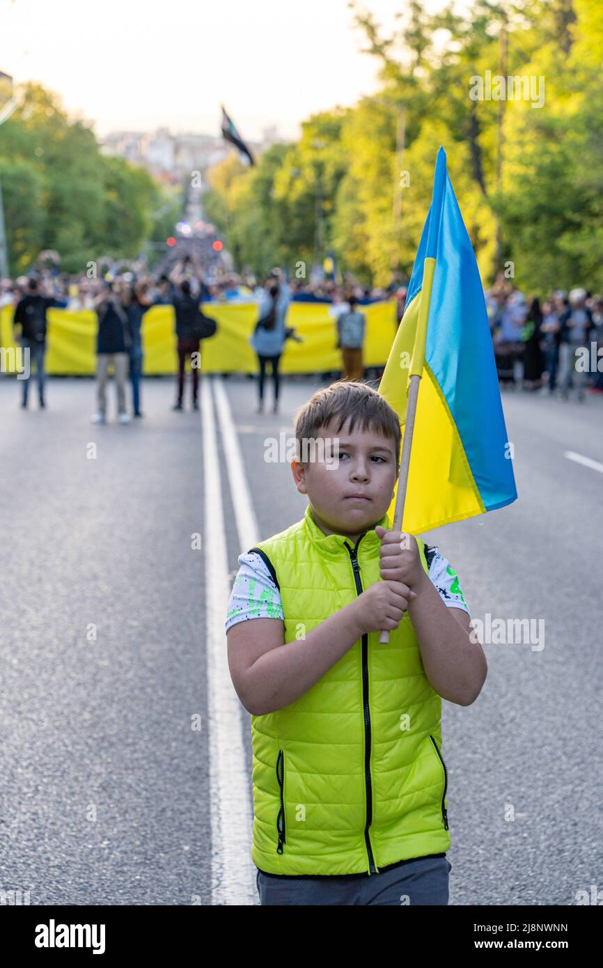 A kid with Ukrainian flag in his hands stands in front of a line of the people walking with a giant flag of Ukraine in Sofia. Bulgaria Stock Photo