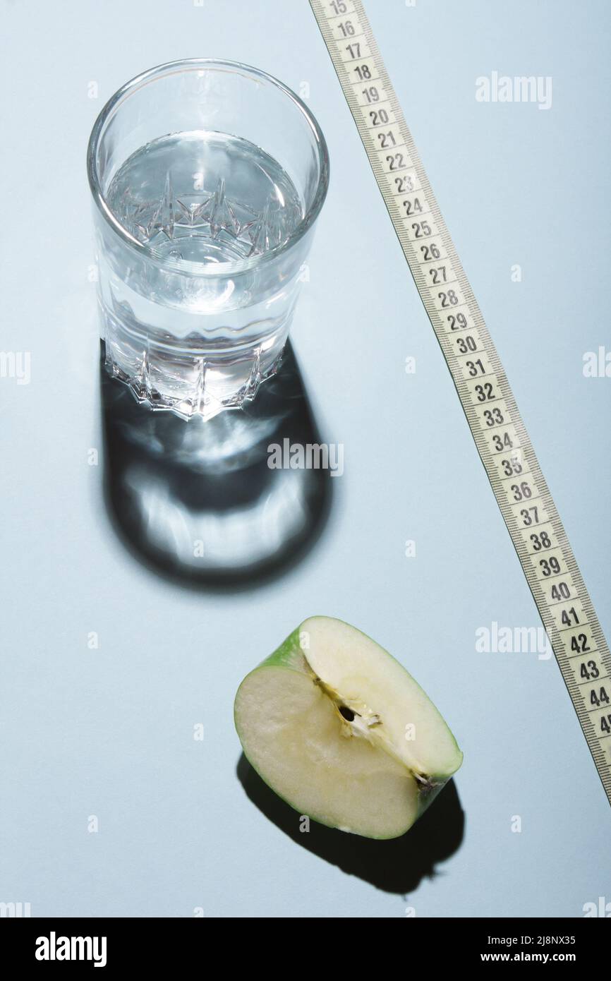 Healthy livestyle diet concept layout. Glass of water with apple slice and a tape measure on blue background. Stock Photo