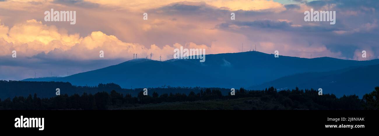 Panoramic view of the Serra da Lousã in Portugal, with the mountain range silhouetted against a background of giant clouds illuminated by the sunset. Stock Photo
