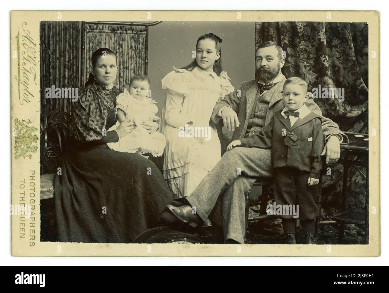 Original Victorian cabinet card studio portrait of attractive prosperous middle or upper middle class Victorian family group, mother and father, daughter, son and baby. It is interesting to see that the woman and girls avert their eyes and the man and boy look confidently at the camera. from the studio of A.G. Taylor, studios in Sunderland & South Shields, Northern England, U.K.  Circa 1895 Stock Photo