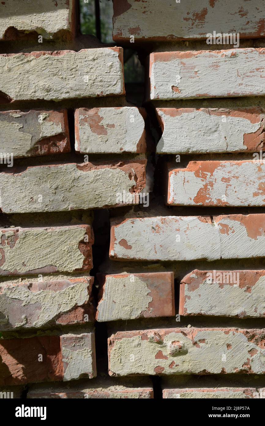 Old brick wall with a vertical crack and peeling plaster Stock Photo