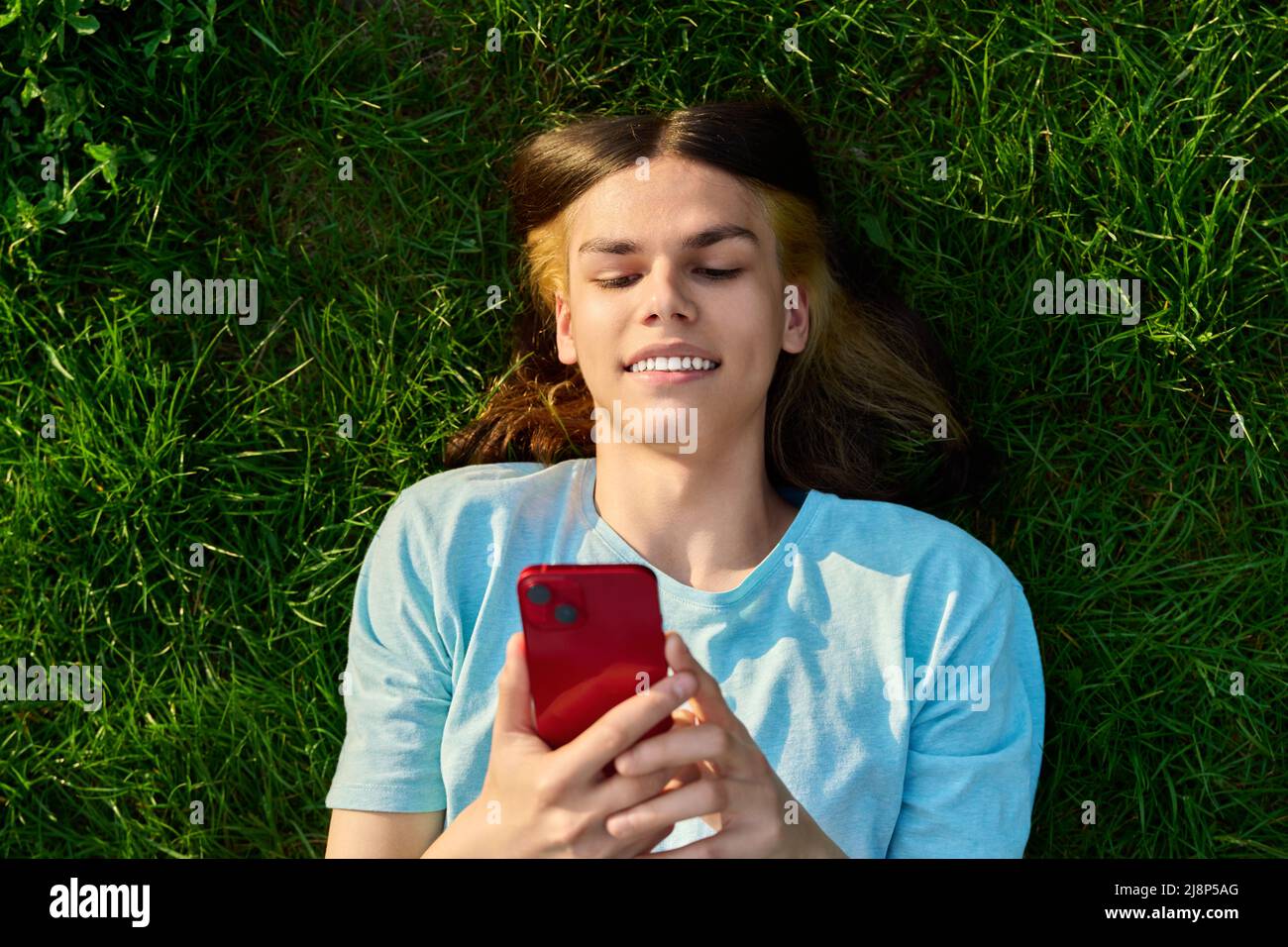 Young guy with smartphone in his hands on green grassy background Stock Photo