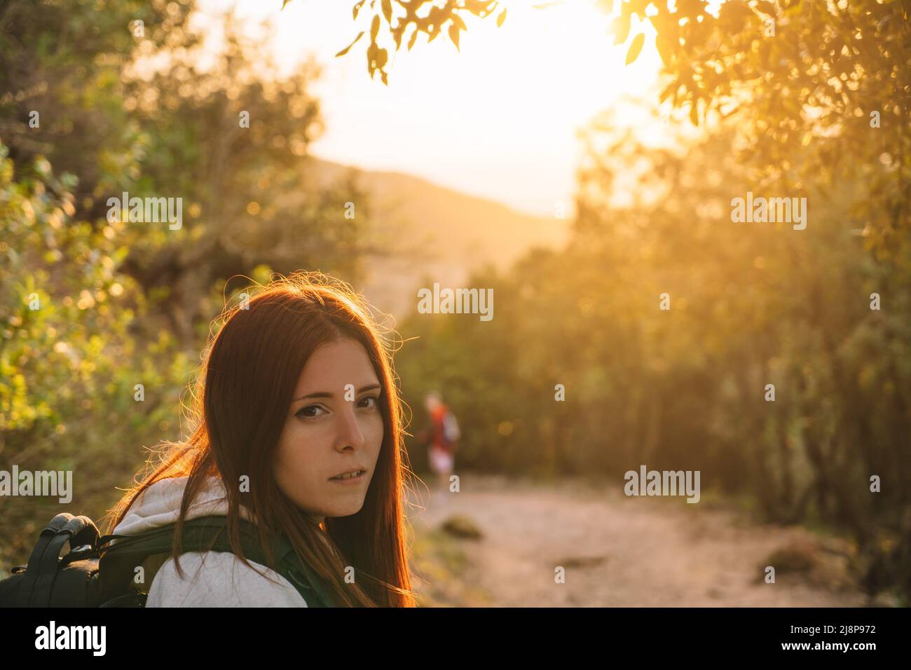 young girl hiker, looking at camera, enjoying the sunset on the mountain. concept of hobby and travel. copy space Stock Photo