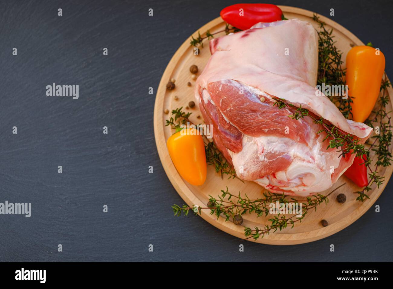 Pork meat on the bone, sweet fresh pepper and thyme herb on a wooden board on a black slate background.Meat products.Farm organic bio meat. Stock Photo