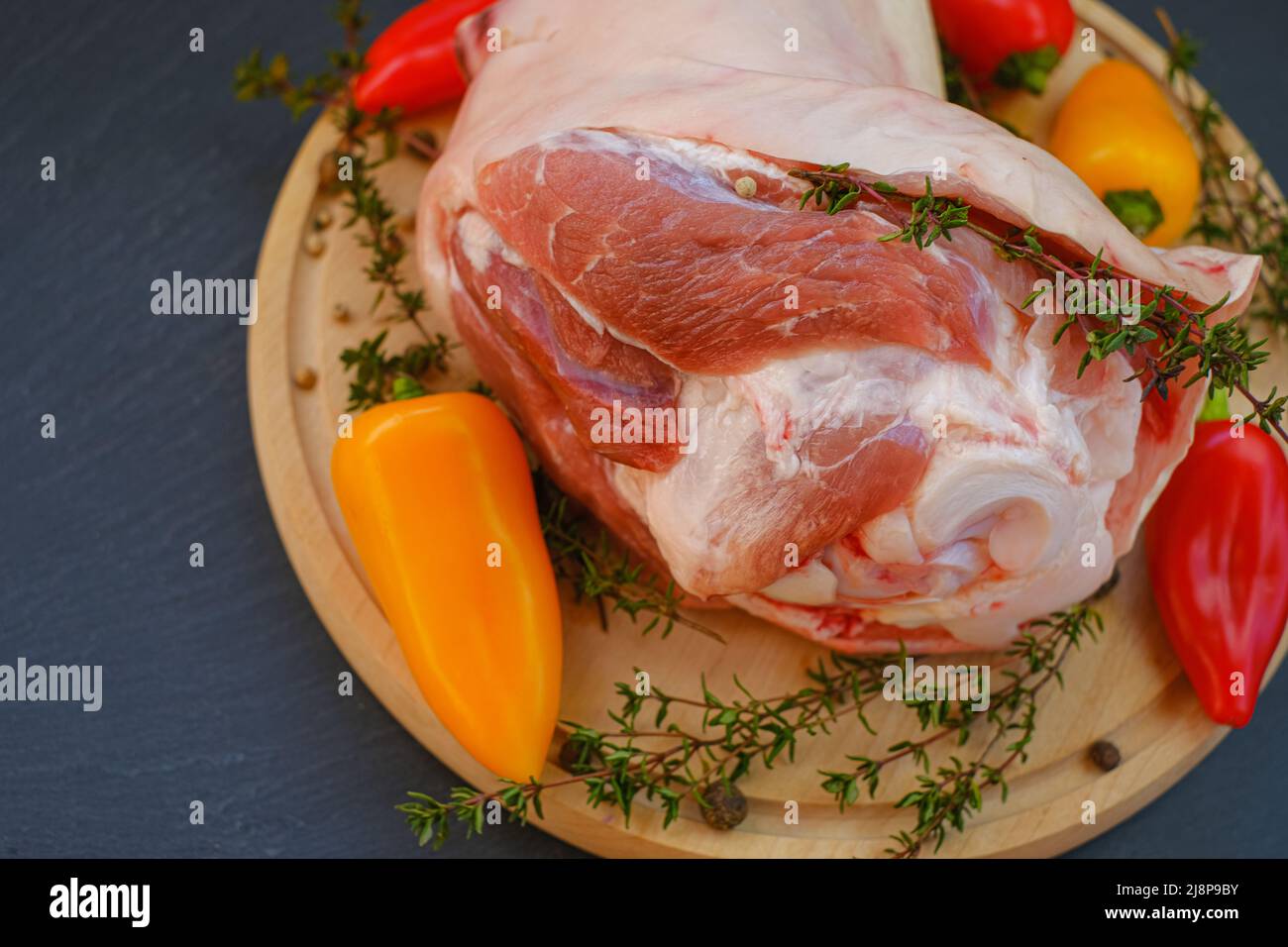 Pork meat on the bone, sweet fresh pepper and thyme herb on a wooden board on a black background.Meat products.Farm organic bio meat. Stock Photo