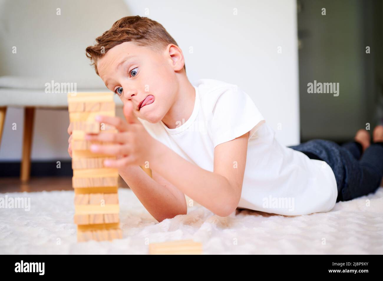 Boy playing wooden block removal tower game at home. Board game Jenga. Kids leisure concept. Stock Photo