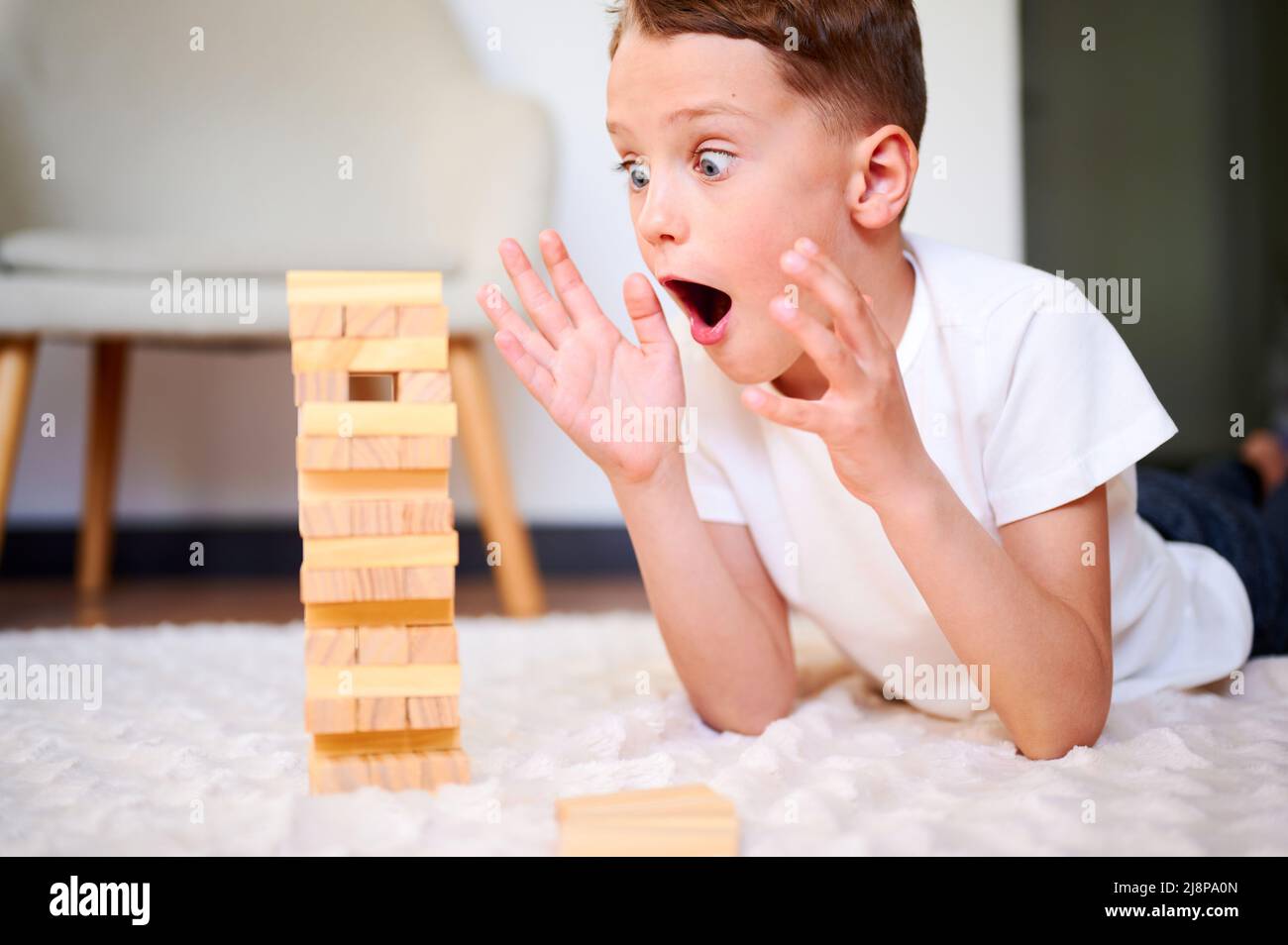 Boy playing wooden block removal tower game at home. Board game Jenga. Kids leisure concept. Stock Photo