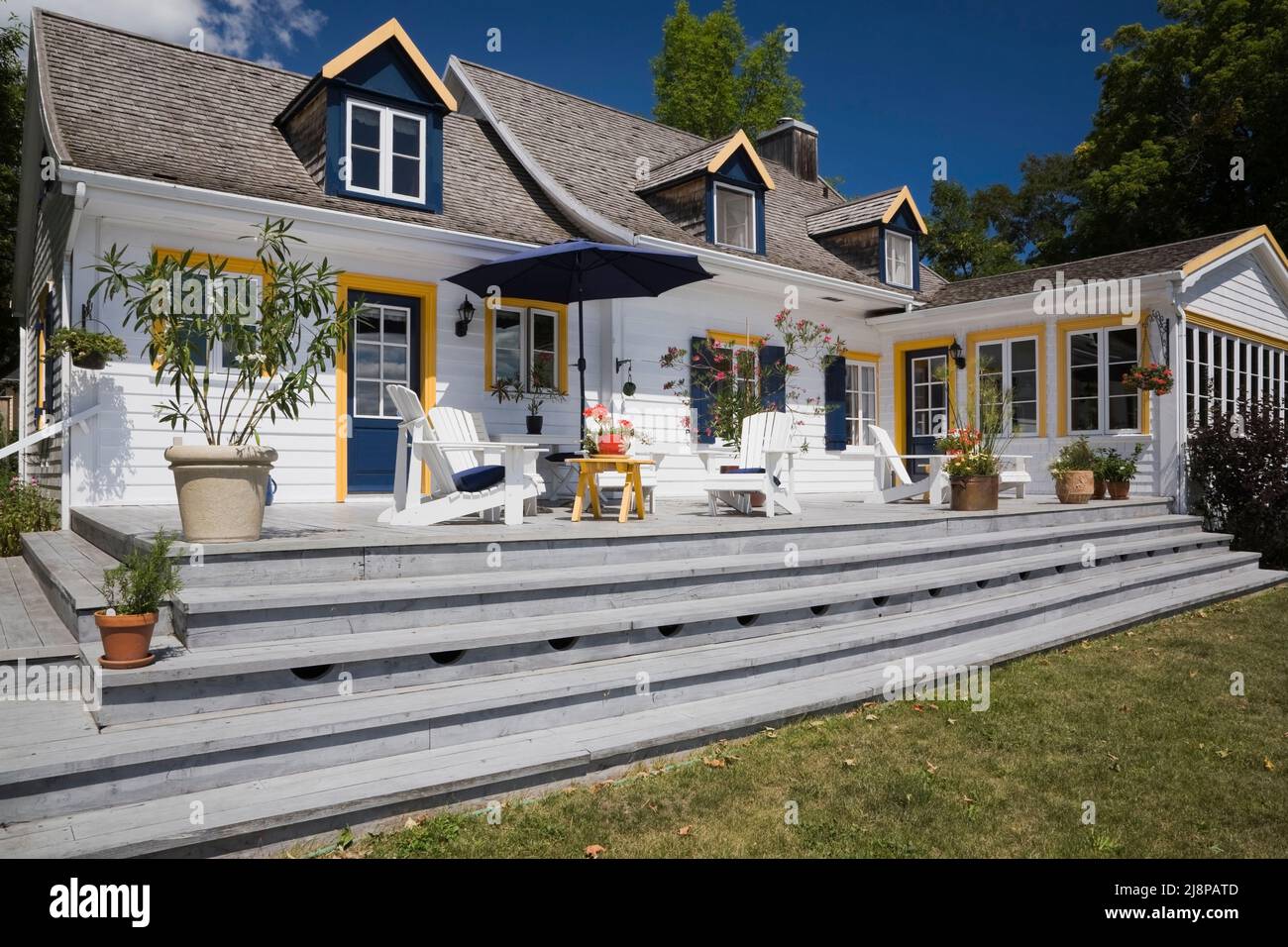 Back of old circa 1830 cottage style home with white wood plank cladding, cedar wood shingles roof and patio deck in summer, Quebec, Canada. This imag Stock Photo