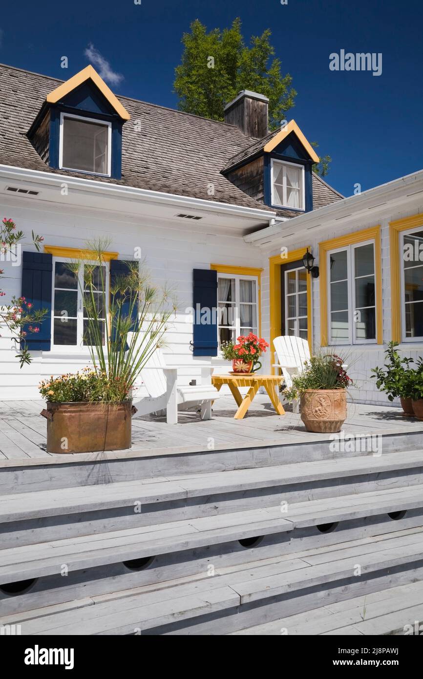 Back of old circa 1830 cottage style home with white wood plank cladding, cedar wood shingles roof and patio deck in summer, Quebec, Canada. This imag Stock Photo