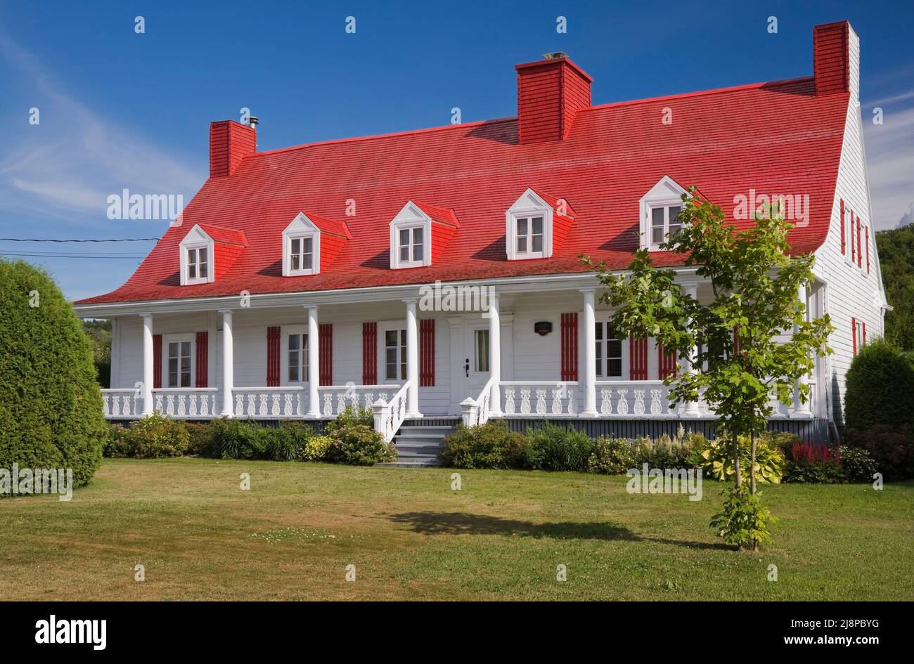Old circa 1825 Canadiana cottage style home with white wood plank cladding and red painted cedar wood shingles roof. Stock Photo