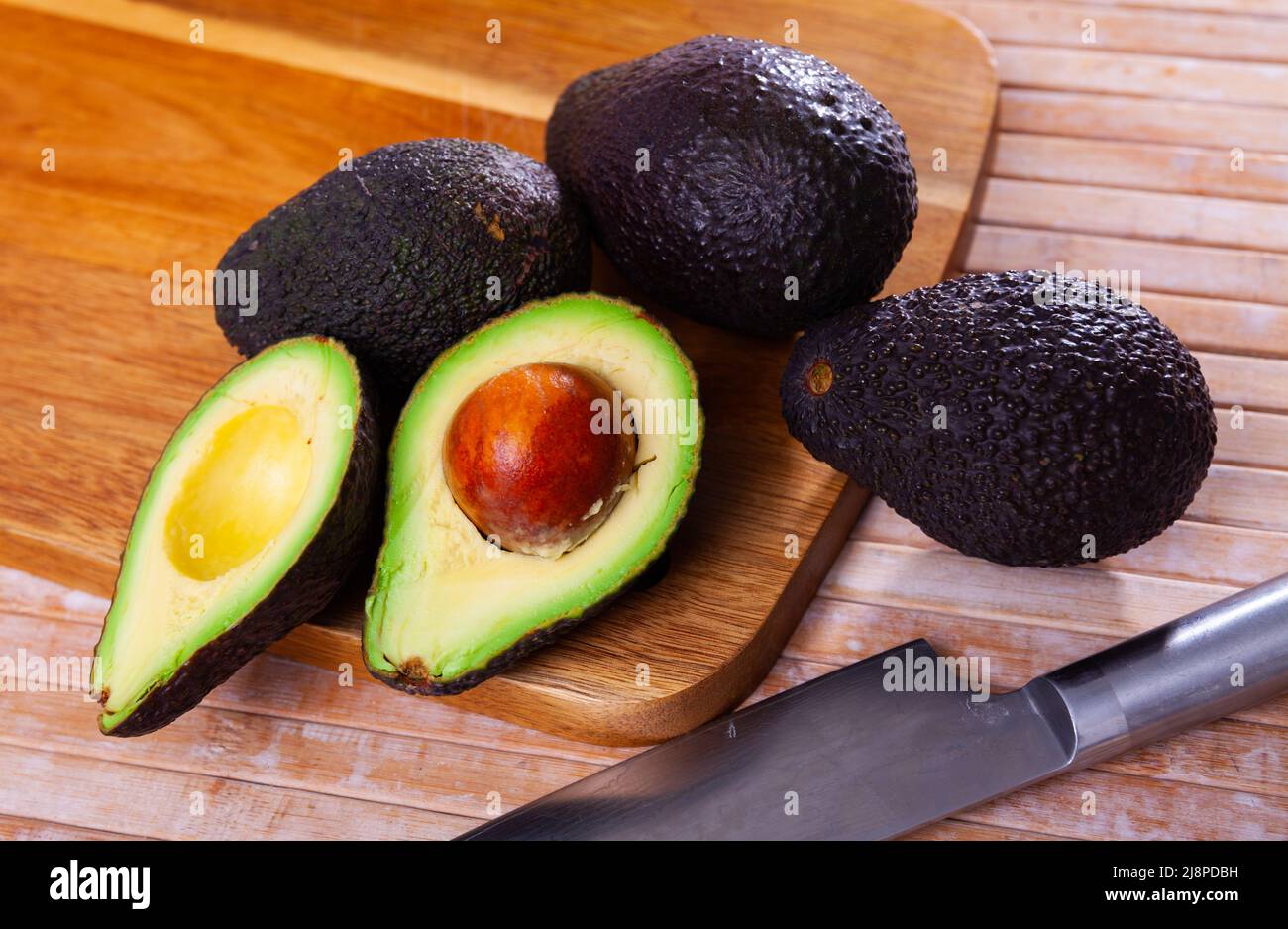 Whole and halved fresh avocados on wooden surface Stock Photo - Alamy