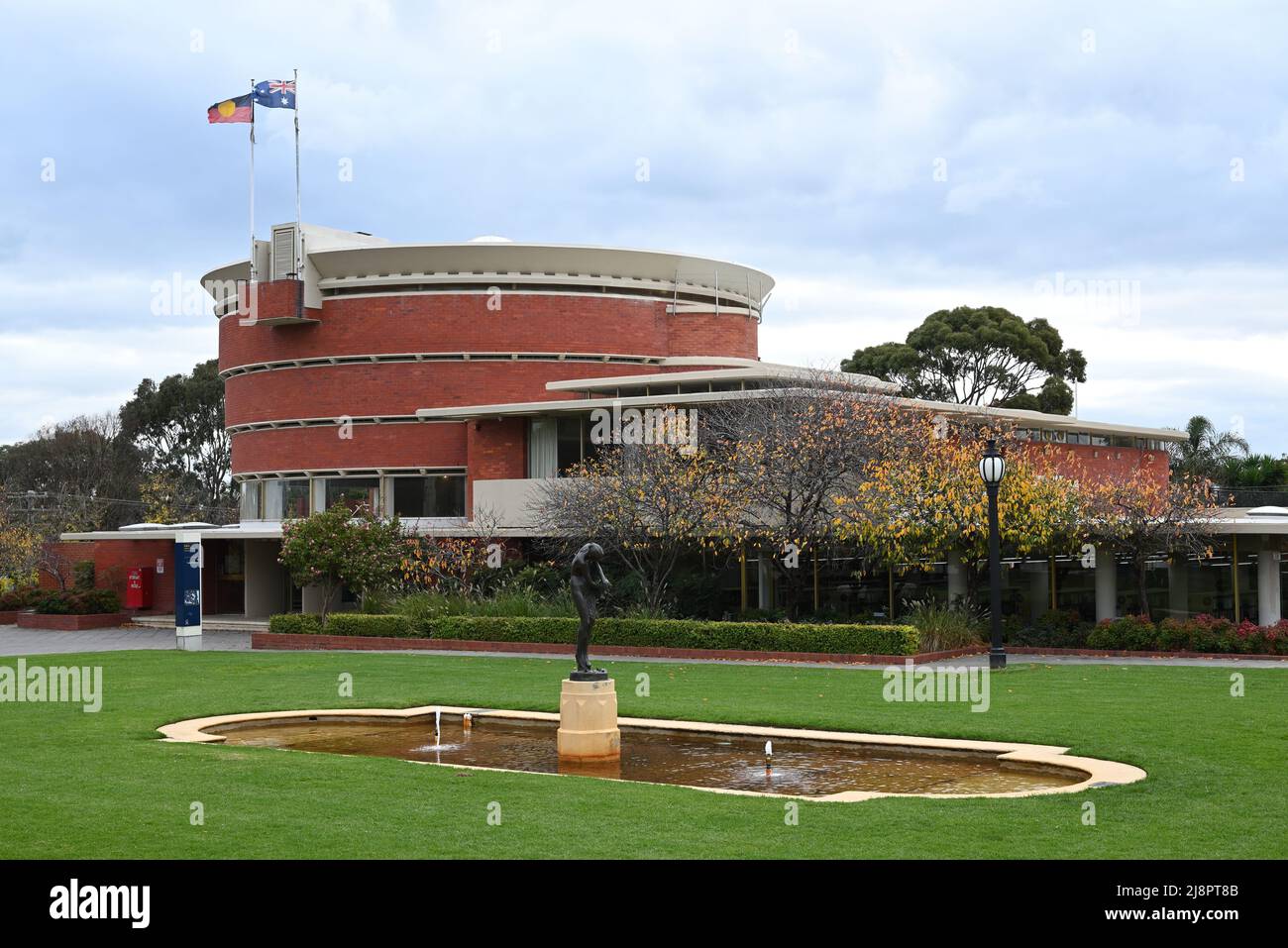 Garden, featuring lawn, a shallow pool, and sculpture, next to circular Bayside Council Chamber and Brighton Library, both in the background Stock Photo