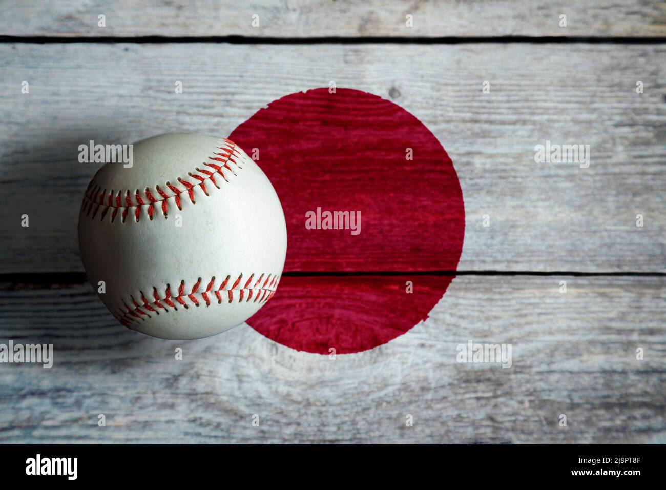 Leather baseball on rustic wooden background painted with Japanese flag with copy space. Japan is one of the top baseball nations in the world. Stock Photo