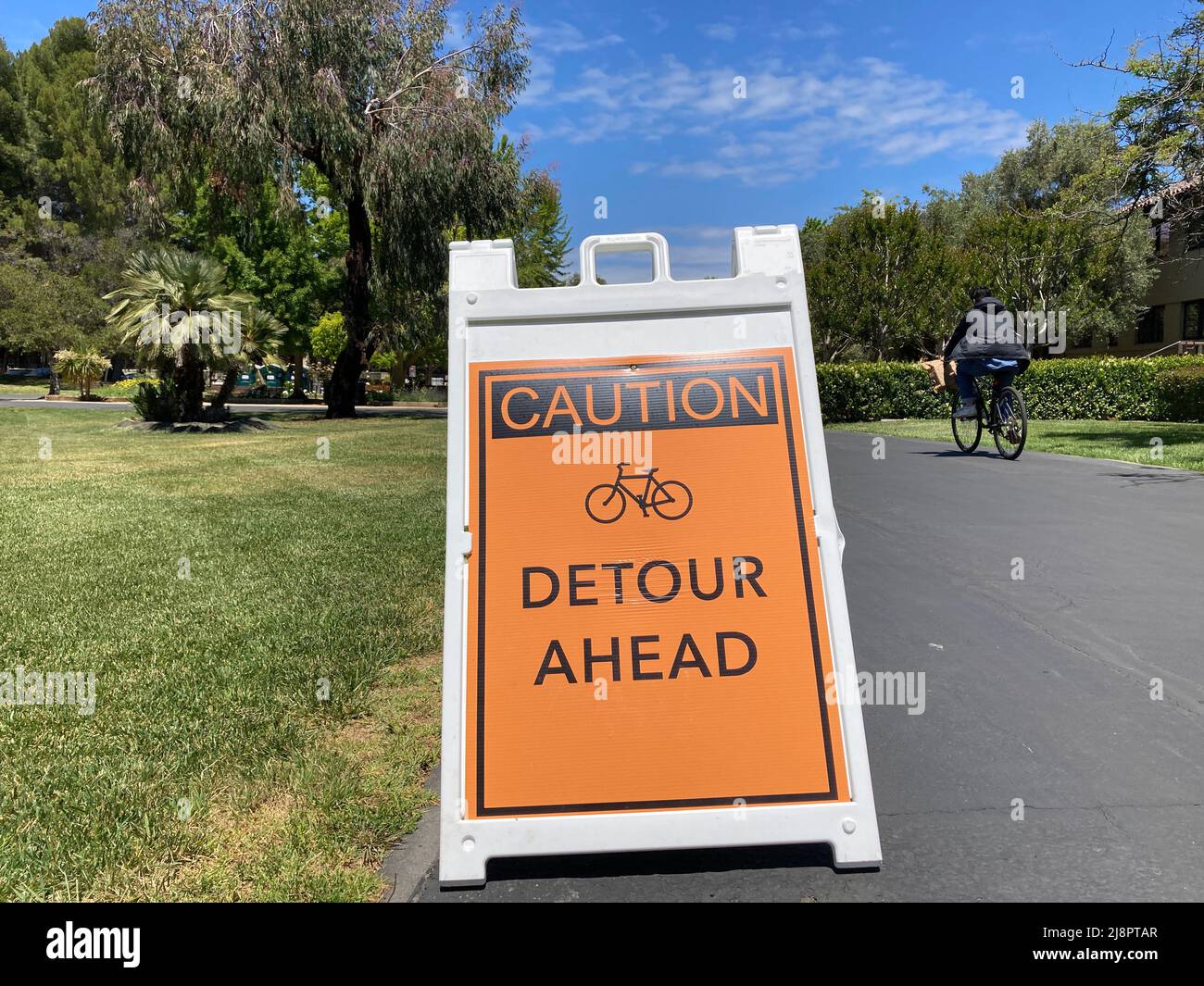 Caution. Detour ahead warning sign with bicycle emblem. Bicyclist is passing by. Stock Photo