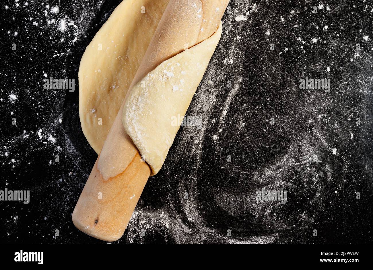 Raw dough  and wooden rolling pin on floured black surface ,baker occupation Stock Photo