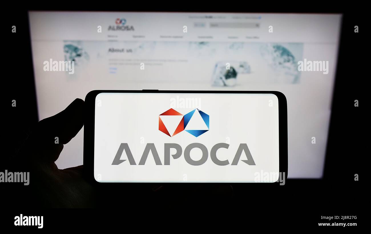 Person holding smartphone with logo of Russian diamond mining company Alrosa PJSC on screen in front of website. Focus on phone display. Stock Photo