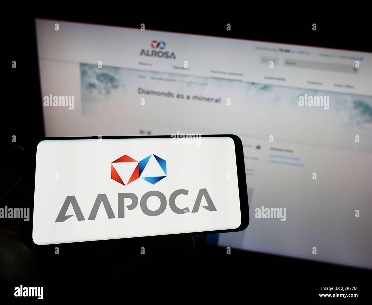 Person holding mobile phone with logo of Russian diamond mining company Alrosa PJSC on screen in front of web page. Focus on phone display. Stock Photo