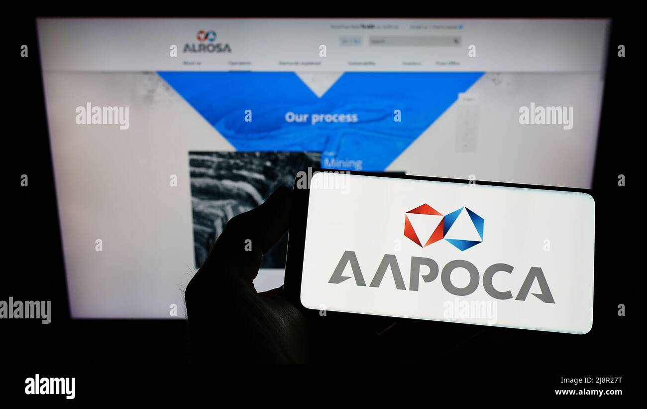 Person holding cellphone with logo of Russian diamond mining company Alrosa PJSC on screen in front of business webpage. Focus on phone display. Stock Photo