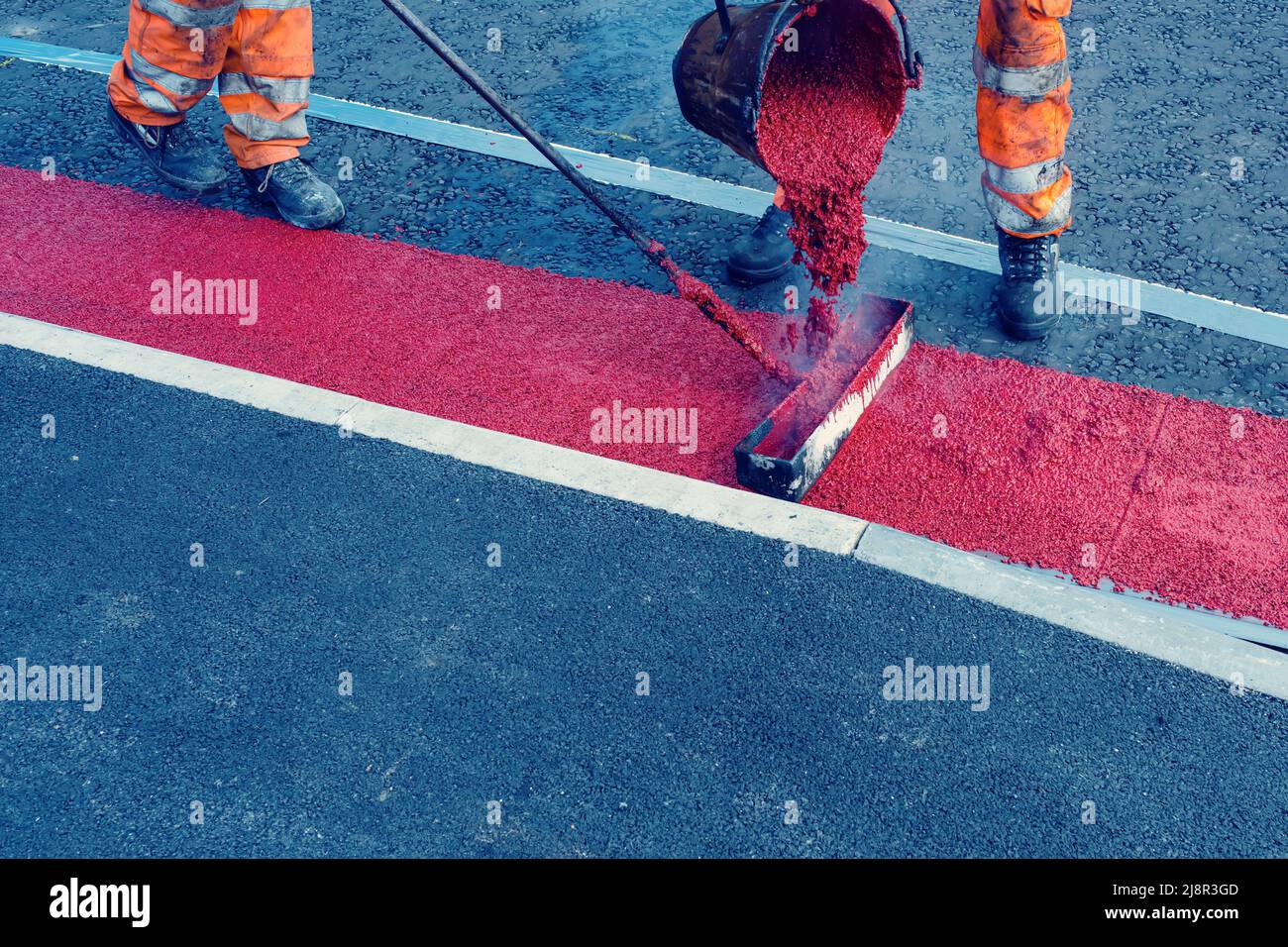 Road workers applying hot red road marking paint on new build road Stock Photo