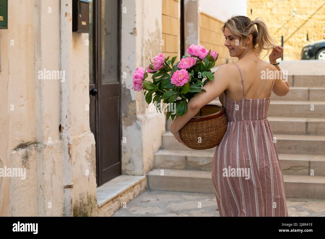 Rearview of attractive blond woman in pink dress holding pot with bouquet of flowers. Herb market. Decoration of houses Stock Photo