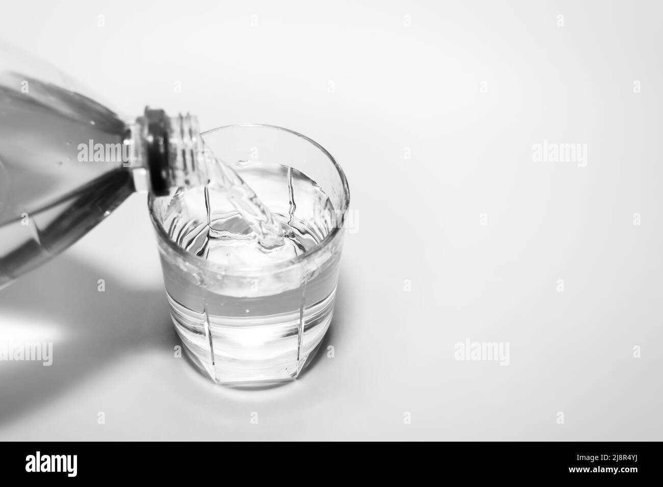 Pouring drinking water into a glass cup from a plastic bottle close-up. Black and white photo. Stock Photo