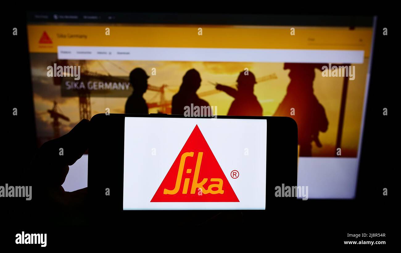 Person holding smartphone with logo of Swiss specialty chemicals company Sika AG on screen in front of website. Focus on phone display. Stock Photo