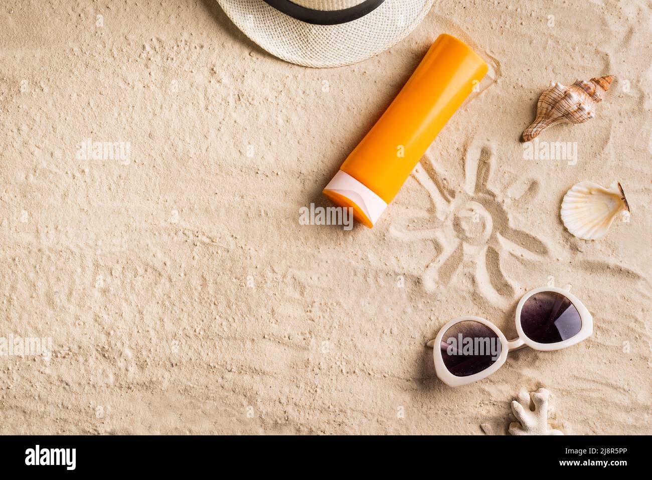 Summer travel beach flat lay composition, copy space. Hat, sunglasses, sunscreen lotion, sunblock cream and seashells on beach sand background. Summer Stock Photo